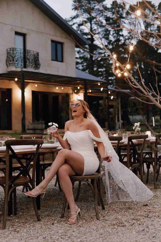 A happy bride sitting outside drinking champagne.