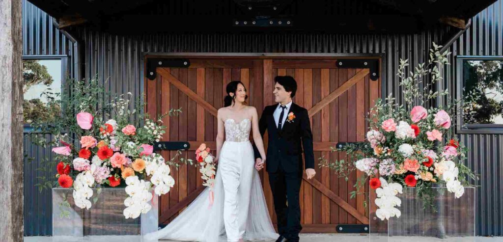 A married couple standing in front of barn doors.