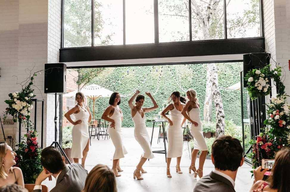 Bridesmaids dancing in warehouse with hedge backdrop
