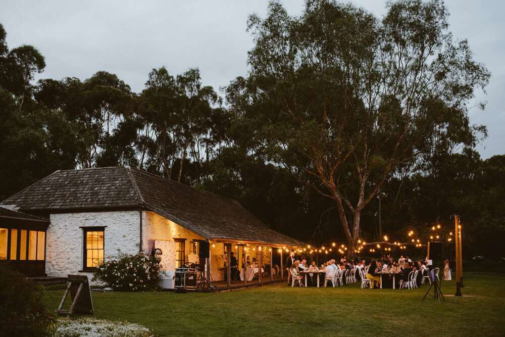 A wedding reception under lights beside a cabin in the woods.
