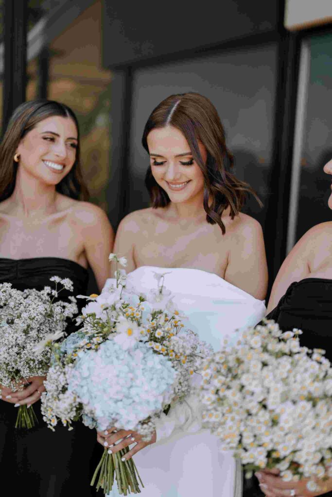 Bride stands with bridesmaids wearing white and holding bouquets of posies