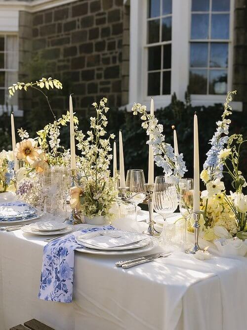 Wedding table topped with white candles, blue and cream florals in vases