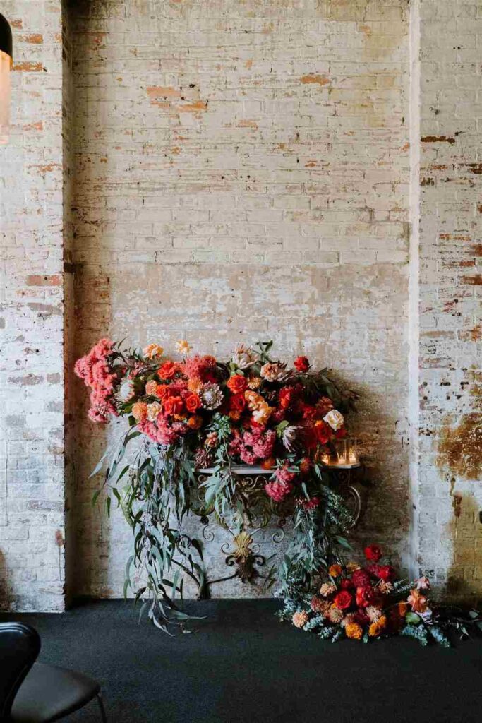 Warm colour floral display with eucalyptus leaves in front of a weathered brick wall
