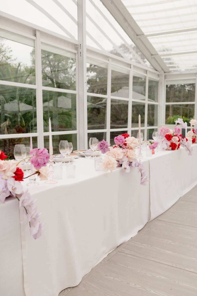 Melbourne wedding bridal party table adorned with candles, glasses and multi-colour flowers of purple pink and red