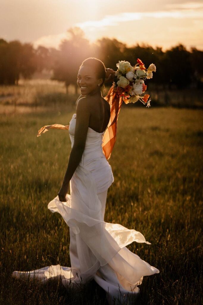 Bride walks into sunset with large bouquet over shoulder with ribbons flowing down