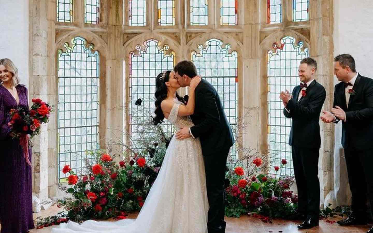 A grand melbourne wedding venue bride and groom kiss in front of window and red flowers