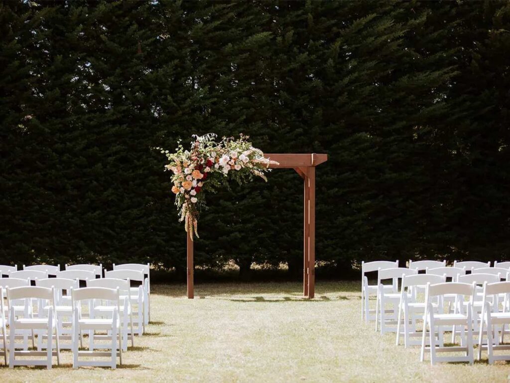 outdoor wedding ceremony with timber square arbour and white chairs