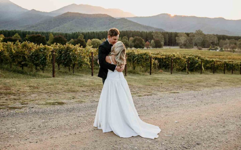 Bride and groom kissing in driveway at winery at sunet.