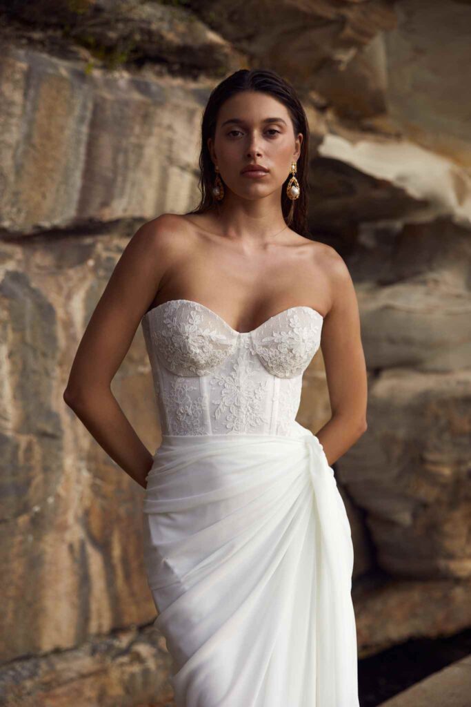 Bride poses for picture in front of stone wall.