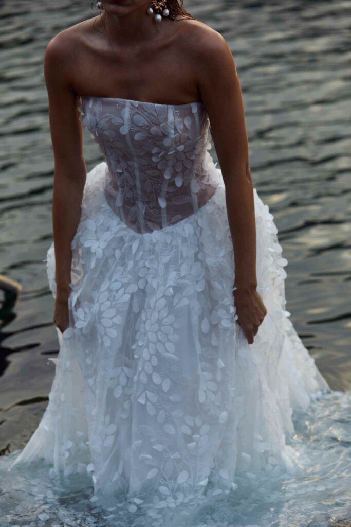 Bride wades across ocean water in floral gown.