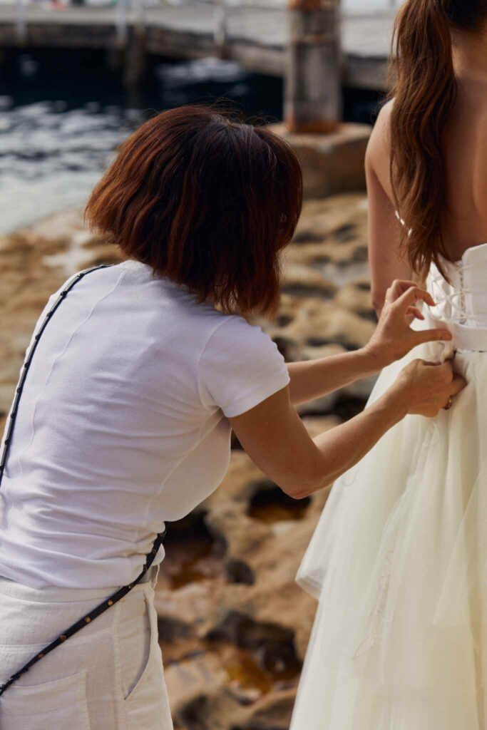 Person fixes strap on the back of a wedding dress.