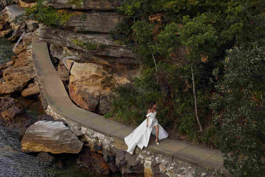 ride walks along ocean-side footpath in wedding gown.