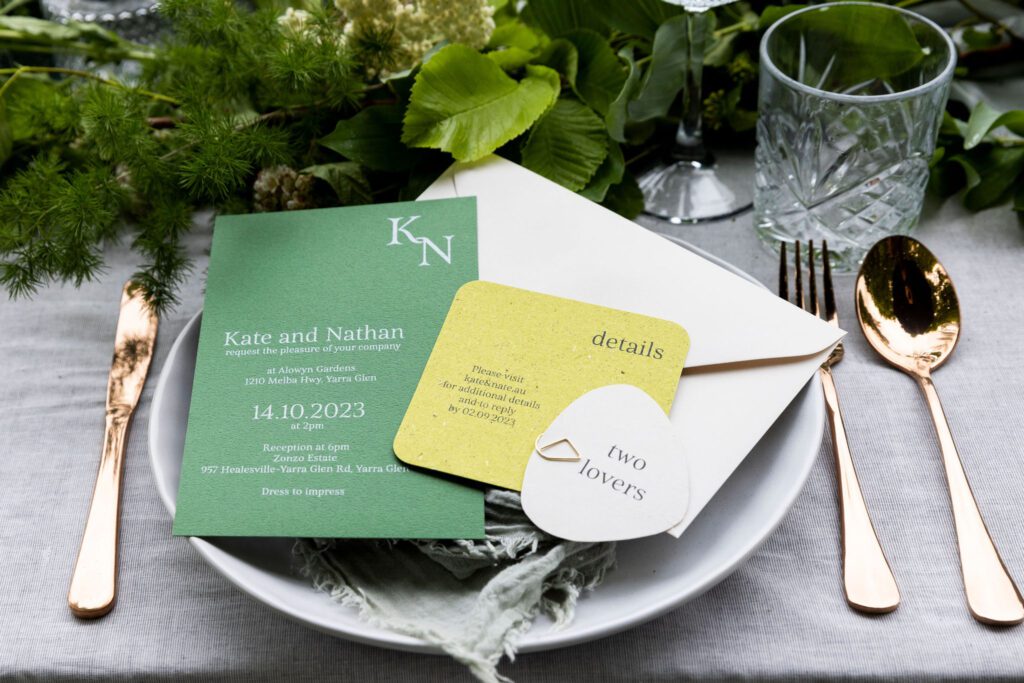 A couple of green-themed wedding invitations on a place setting.