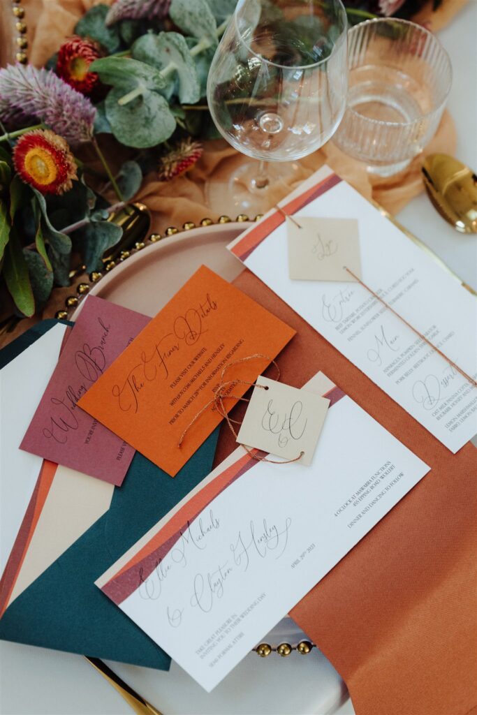 A couple of orange, red and green wedding invitations on a place setting.