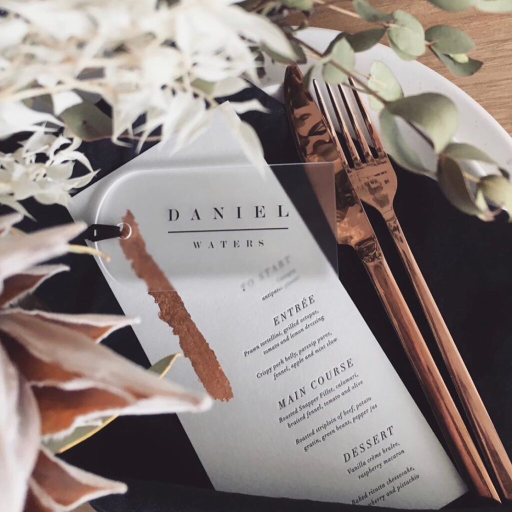 A name tag lying on top of a wedding menu on a place setting.