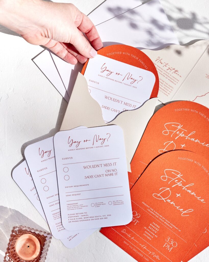 A series of orange wedding invitations and RSVPs in an envelope