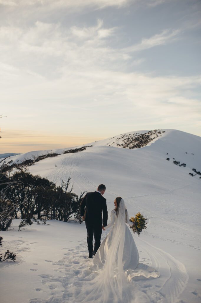 Couple walking along snow holding hnads