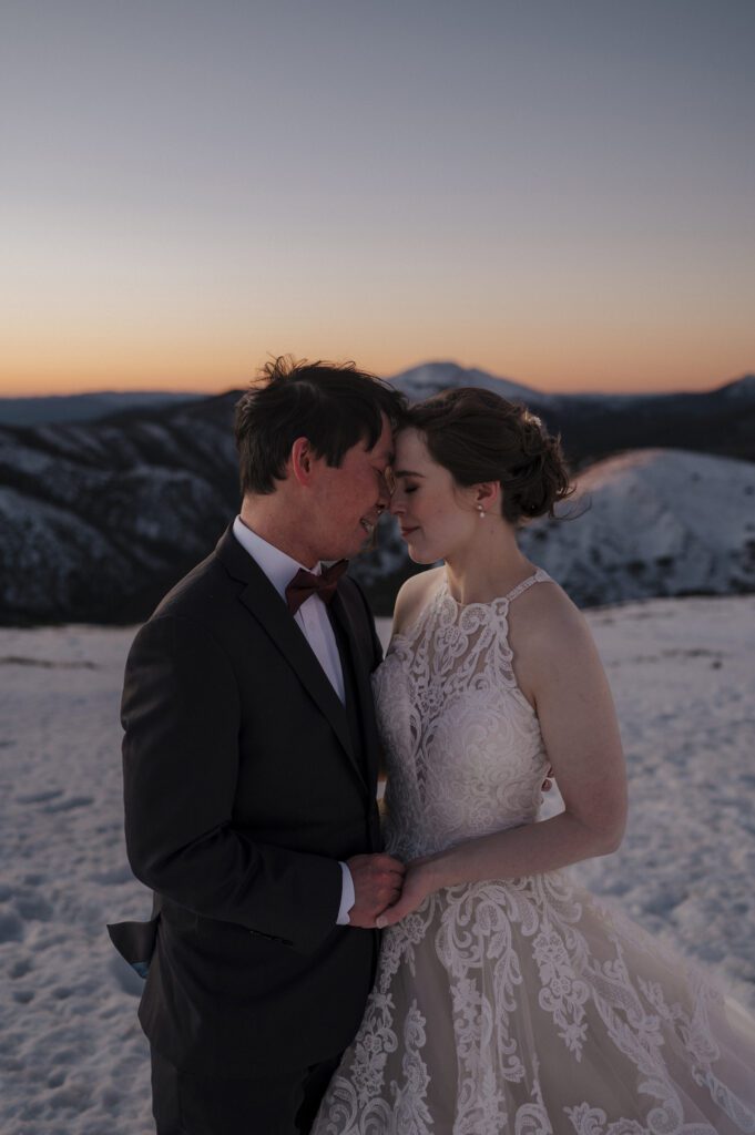 Bride and groom looking into each others eyes at sunset at snow